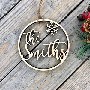 May include: A wooden Christmas ornament with the text "the Smiths" and a snowflake cutout. The ornament is brown and has a string for hanging.