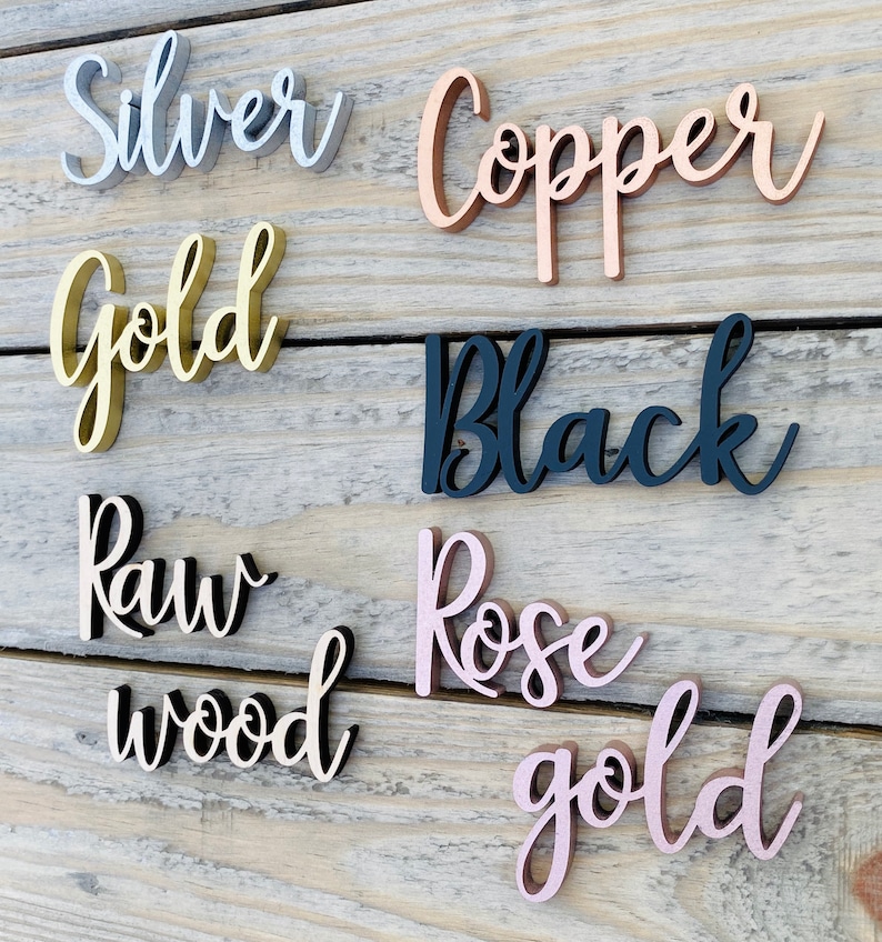 K&ouml;nnte beinhalten: Nahaufnahme von sechs Holzschildern mit verschiedenen Oberfl&auml;chen. Die Schilder zeigen "Silber", "Kupfer", "Gold", "Schwarz", "Rohholz" und "Ros&eacute;gold".