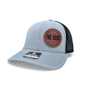 May include: A gray and black trucker hat with a brown leather patch that says "Because I'm The Boss That's Why".