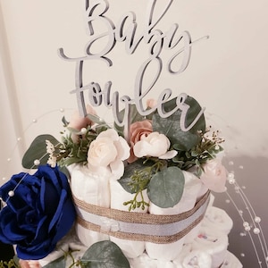 May include: A diaper cake decorated with blue and pink flowers, greenery, and a wooden sign that says "Baby Shower".