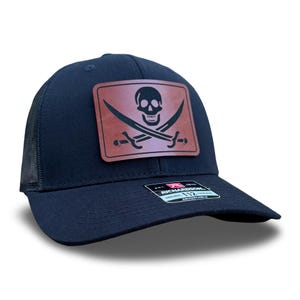 May include: A black trucker hat with a brown leather patch featuring a skull and crossbones design. The hat is adjustable and has a mesh back.