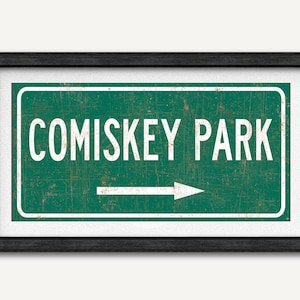 May include: A green and white vintage-style road sign with a white arrow pointing to the right. The sign reads "Comiskey Park".