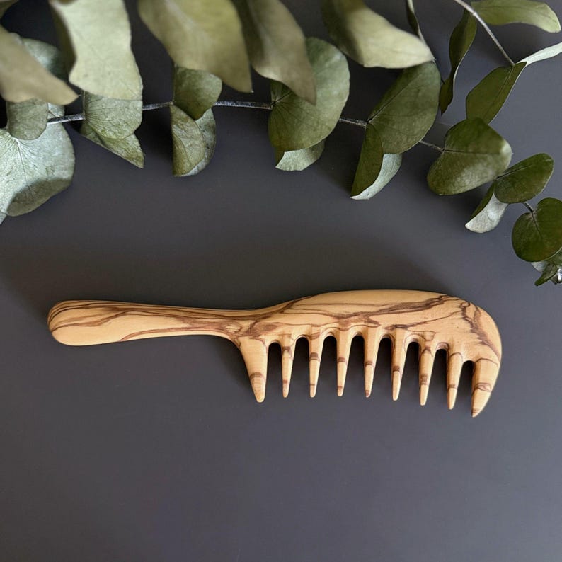 May include: A wooden comb with a natural wood grain pattern. The comb has a wide handle and a row of teeth.