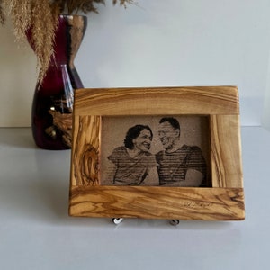 May include: A wooden picture frame with a natural wood finish. The frame has a raised edge and a cutout for a photo. A black and white photo of a couple is visible in the frame. The date "02 09 2023" is engraved on the bottom of the frame.