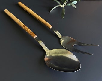 May include: A set of two kitchen utensils with olive wood handles. The utensils are a serving spoon and a fork. The spoon has a rounded bowl and the fork has two tines.