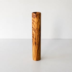 May include: A cylindrical vase made of olive wood. The vase has a natural wood grain pattern in shades of brown and tan. The vase is standing upright against a white background.