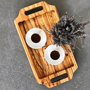 May include: A wooden serving tray with two handles on each side. The tray is made of light brown wood with dark brown streaks. There are two white ceramic cups with coffee on the tray. A bouquet of dried lavender is on the tray.