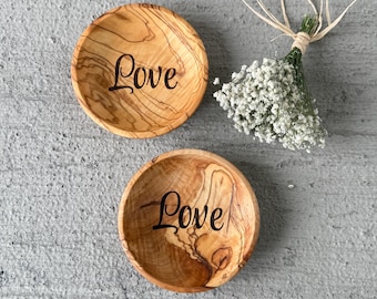 May include: Two small wooden bowls with the word "Love" engraved on them. The bowls are made of olive wood and have a natural wood grain.