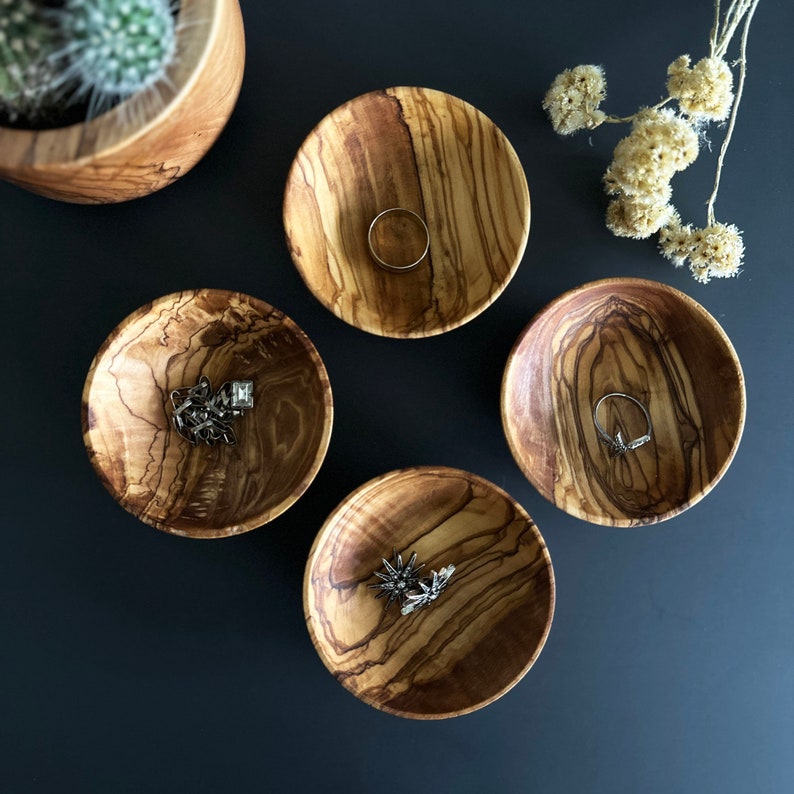 May include: Four small wooden bowls with natural wood grain patterns. Each bowl has a different design and is filled with jewelry, including rings and a chain.