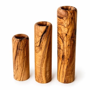 May include: Three cylindrical vases made of olive wood. The vases vary in height, with the tallest measuring approximately 10 inches. The wood grain is visible, showcasing a mix of light and dark brown tones. The vases have a smooth, polished finish.