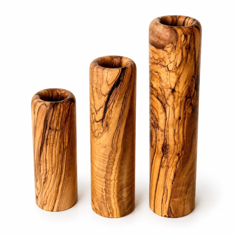 May include: Three cylindrical vases made of olive wood. The vases vary in height, with the tallest measuring approximately 10 inches. The wood grain is visible, showcasing a mix of light and dark brown tones. The vases have a smooth, polished finish.