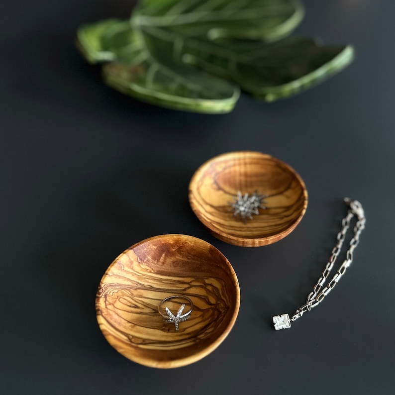 May include: Two small wooden bowls with a natural wood grain pattern. One bowl contains a silver ring with a star-shaped design. The other bowl contains a silver chain with a star-shaped pendant.