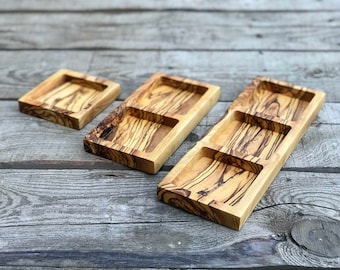 May include: Three wooden serving trays with different sizes and shapes. The trays are made of olive wood and have a natural finish. The largest tray has three compartments.