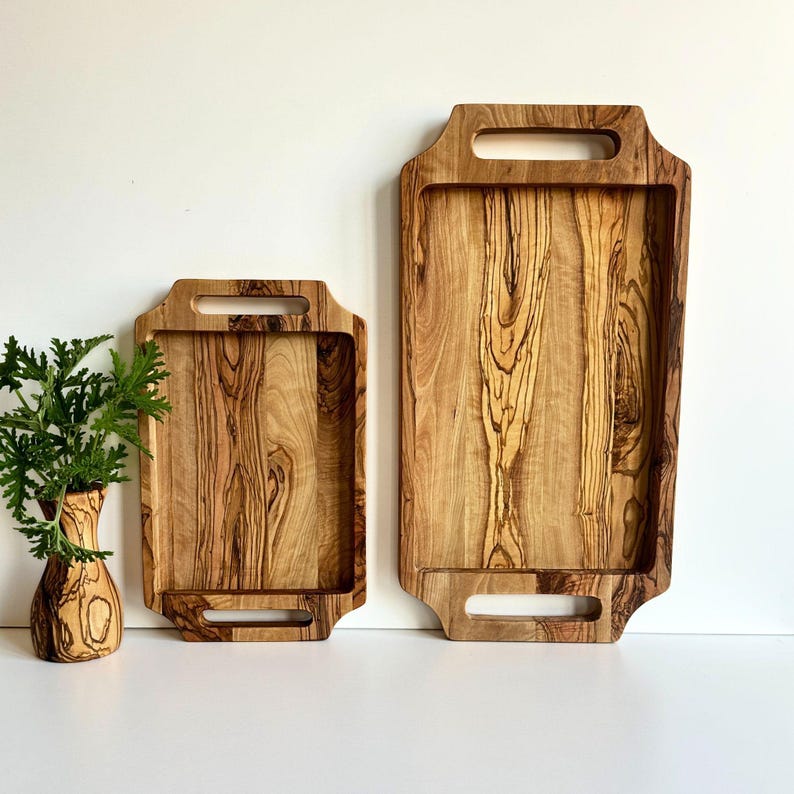 May include: Two wooden serving trays with handles. The trays are made of light brown wood with dark brown streaks. The larger tray is about 12 inches long and the smaller tray is about 8 inches long.