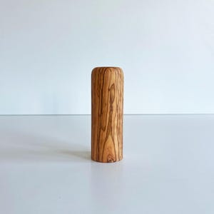 May include: A cylindrical wooden object with a rounded top. The wood has a natural grain pattern in shades of brown and tan. The object is standing upright against a white background.