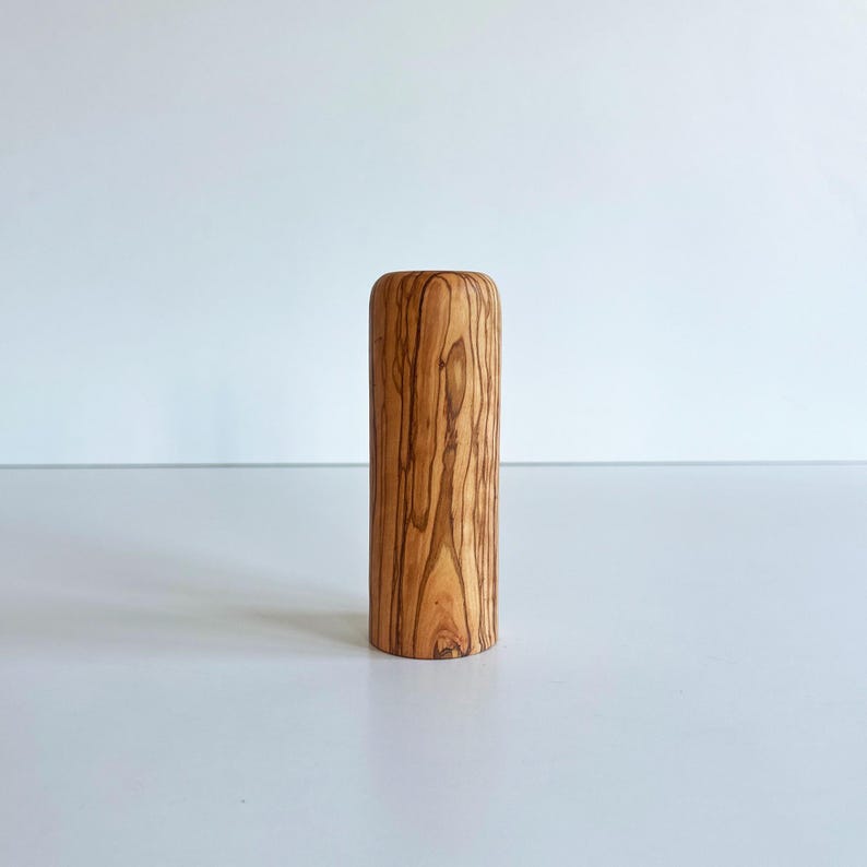 May include: A cylindrical wooden object with a rounded top. The wood has a natural grain pattern in shades of brown and tan. The object is standing upright against a white background.