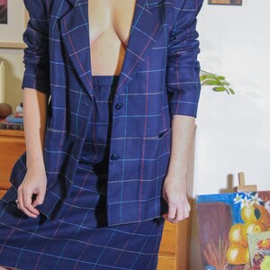 May include: A blue plaid blazer and skirt set with a red, blue, and white plaid pattern. The blazer has a notched collar and two pockets. The skirt is knee-length.