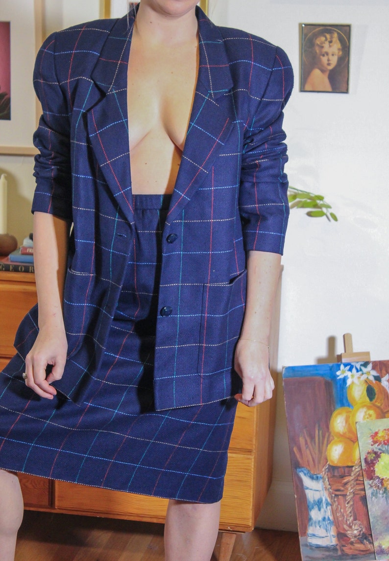 May include: A blue plaid blazer and skirt set with a red, blue, and white plaid pattern. The blazer has a notched collar and two pockets. The skirt is knee-length.