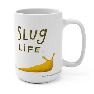 May include: White ceramic mug with the words "SLUG LIFE" in green and a yellow cartoon slug illustration. The mug has a large handle and is suitable for hot or cold beverages.