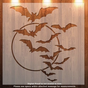 May include: A stencil featuring a design of bats flying around a full moon. The stencil is made of a white material and is placed on a wooden background.