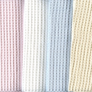 May include: Close-up of a textured fabric with a waffle weave pattern. The fabric is divided into vertical stripes of varying colours, including pink, white, light blue, and beige. The texture is consistent throughout.