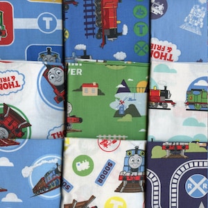 May include: A collection of eight fabric squares featuring Thomas the Tank Engine and his friends. The squares are in various colours, including blue, green, white, and red. Each square features a different design, including trains, tracks, and the words "Thomas & Friends" and "Sodor".