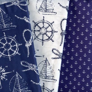 Può includere: Tre tessuti a tema nautico con illustrazioni bianche su sfondi blu navy e bianchi. I disegni includono barche a vela, ruote di navi, ancore e nodi di corda. I tessuti sono probabilmente in cotone o lino.