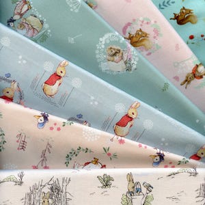 Może przedstawiać: Pięć różnych próbek tkanin z powtarzającym się wzorem postaci z Peter Rabbit w leśnym otoczeniu. Tkaniny są w odcieniach niebieskiego, różowego i białego.