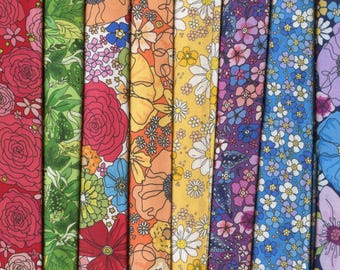 May include: Eight vertical strips of fabric featuring diverse floral patterns in red, green, orange, yellow, purple, and blue. Each strip displays a unique botanical print with various flower shapes, leaves, and stems in vibrant colors.