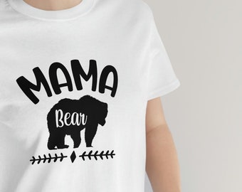 May include: White t-shirt with black text that reads "Mama Bear" and a black silhouette of a bear. The bear has the word "Bear" written on its back.