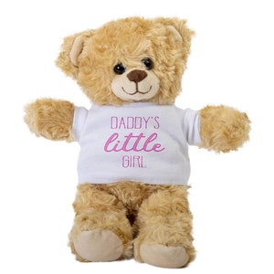May include: A light brown teddy bear wearing a white t-shirt with the text "Daddy's little girl" in pink lettering.