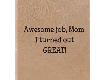 May include: A tan notebook with a textured cover. The text "Awesome job, Mom. I turned out GREAT!" is printed in black, centered on the front. The notebook is rectangular in shape and is a light brown colour.