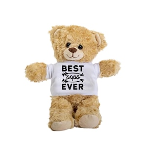 Puede incluir: Un oso de peluche marrón que lleva una camiseta blanca con el texto "BEST oops EVER" impreso en negro.