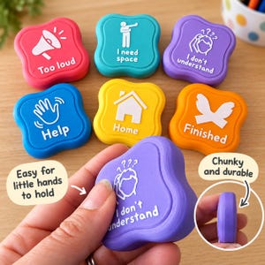 May include: A set of seven colourful, square-shaped communication buttons with rounded corners. Each button features a white icon and text, including phrases like Too loud, I need space, I don't understand, Help, Home, and Finished in various colours.