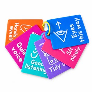 May include: A set of colourful plastic cards held together by a yellow ring. Each card features white text and simple line icons. The cards include phrases such as Eyes this way, Sit nicely, Tidy up, Good listening, Quiet voice, and Hands to myself.