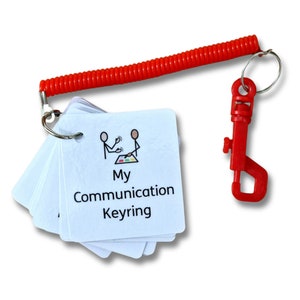 May include: A white keychain with a red coil strap and a red clip. The keychain has a stack of cards with a simple illustration of two people playing a game and the text "My Communication Keyring".