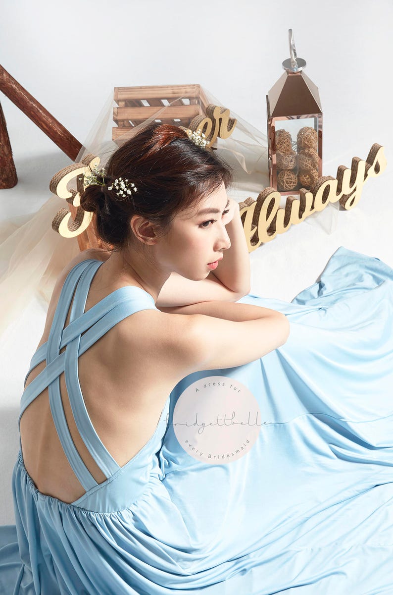 May include: A light blue bridesmaid dress with a criss-cross back detail. The dress is made of a soft, flowing fabric and has a simple, elegant design. The text "A dress for every bridesmaid" is visible on the dress.