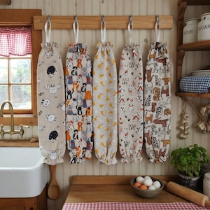 May include: Five fabric bag dispensers hanging on a wooden rack. Each bag has a different pattern, including sheep, cats, and dogs. The bags are beige, white, and brown. The text "DOGS LIFE" is printed on one of the bags.