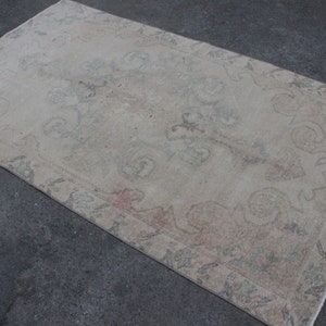 Könnte beinhalten: Ein vintagefarbener, cremefarbener Teppich mit einem verblassten Blumenmuster und einem dezenten Farbspiel in Rosa und Grün. Der Teppich hat einen abgenutzten Look und einen Fransenrand.