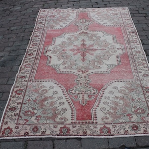 May include: A vintage Turkish rug in pink and cream with a floral pattern and a central medallion. The rug is in good condition with some signs of wear and tear.