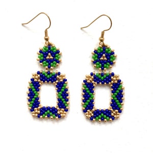 Puede incluir: Un par de pendientes colgantes con un componente superior circular y uno inferior rectangular, ambos elaborados con pequeñas cuentas azules, verdes y doradas metálicas. Los pendientes cuelgan de ganchos de metal en tono dorado.