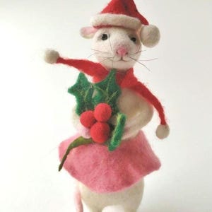 May include: A white felt mouse wearing a red Santa hat and a pink skirt, holding a sprig of holly with red berries.