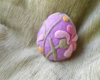 May include: A purple felt Easter egg with a floral design. The egg is decorated with green leaves, pink flowers, and yellow dots.