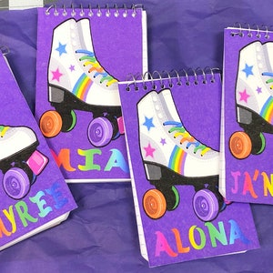 May include: Purple spiral notebooks with a roller skate design. The white skates have rainbow laces and accents, with colorful wheels. Each notebook has a name printed in rainbow colors: J'Myre, Mia, Alona, and Ja'Niyah.