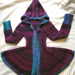 May include: A purple, blue, and green striped crocheted hooded cardigan with a long, flowing hem.