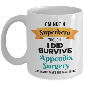 May include: White ceramic coffee mug with a black and teal design. The mug reads "I'm not a superhero though I did survive appendix surgery (OK. maybe that's the same thing)"