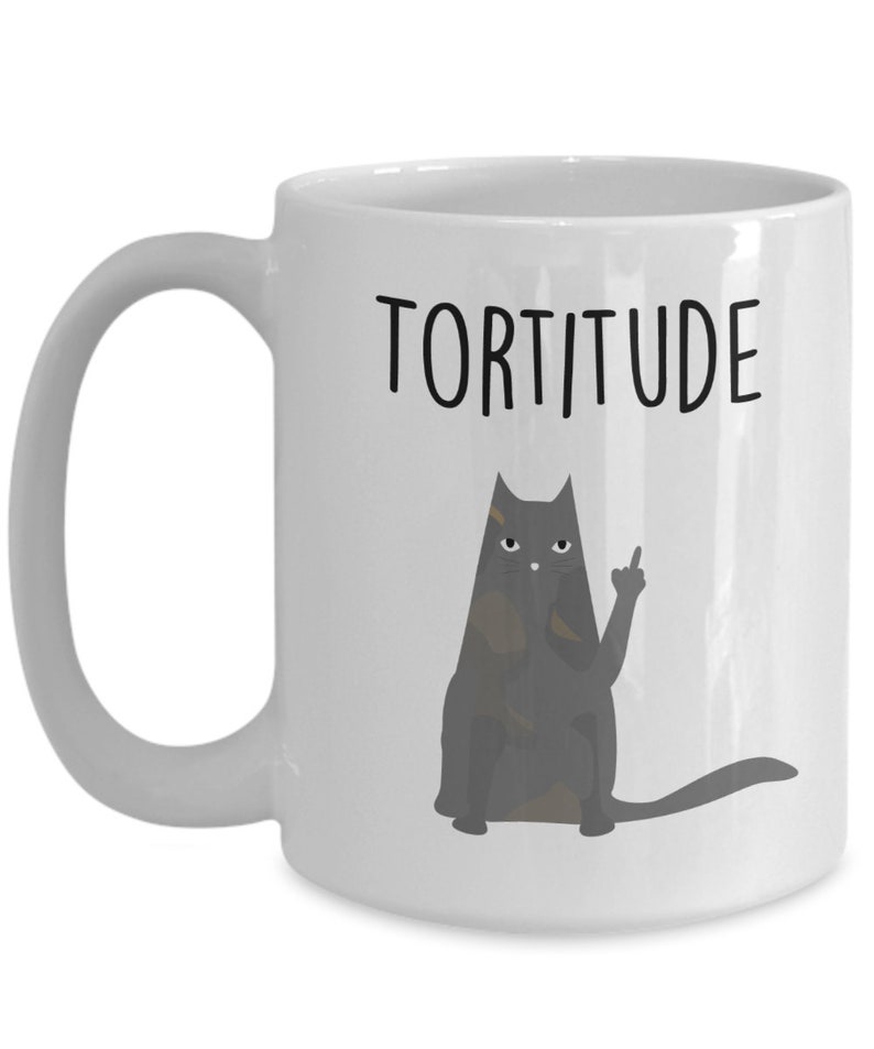 以下が含まれることがあります： 白いセラミック製のコーヒーカップ。黒い猫のイラストと「TORTITUDE」という文字が印刷されています。