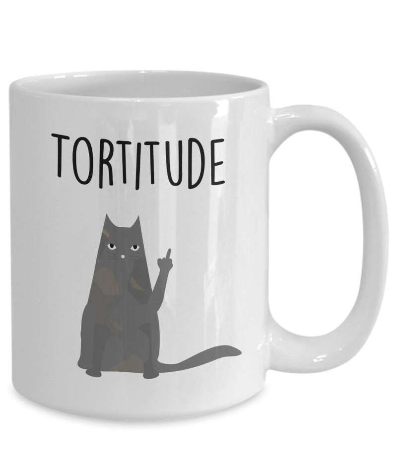 以下が含まれることがあります： 白いセラミック製のコーヒーカップ。黒い猫のイラストと「Torttitude」という文字が印刷されています。