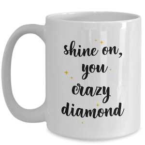 May include: White ceramic coffee mug with a black inscription that reads "shine on, you crazy diamond" with gold glitter accents.