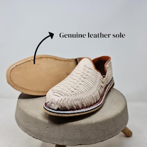 May include: A white ceramic mug with a black handle and the text "But First, Coffee" in a black, handwritten-style font. The mug is on a white surface.